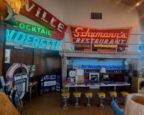 A retro diner interior featuring colorful neon signs, vintage decor, and yellow stools at a counter.