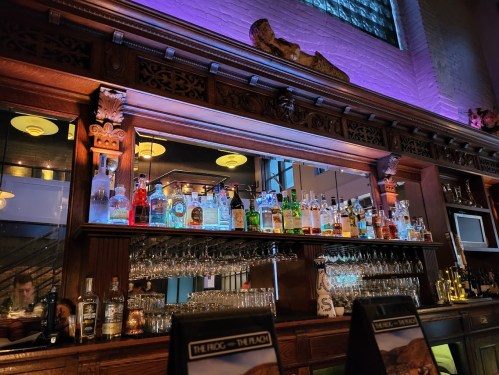 A wooden bar with an ornate design, showcasing a variety of colorful liquor bottles and glassware.