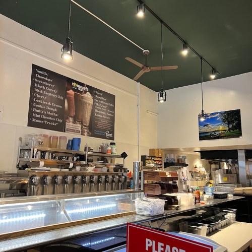 Interior of a café with a menu on the wall, a counter with drinks, and a sign that says "Please Wait to Be Seated."