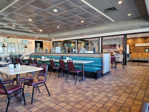 A spacious diner interior with teal booths, red chairs, and tiled flooring, featuring empty tables and a welcoming atmosphere.
