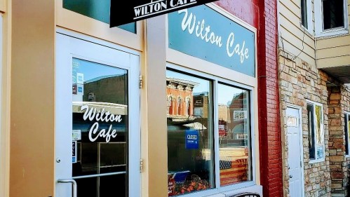 Exterior of Wilton Cafe with a sign above the entrance and reflections of buildings in the windows.