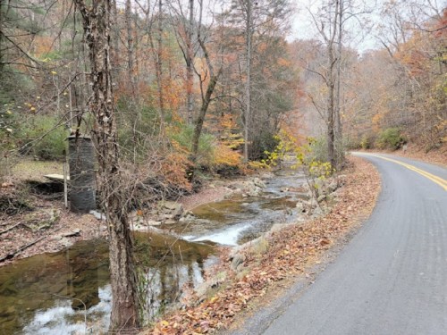 A winding road alongside a creek, surrounded by autumn foliage and bare trees.