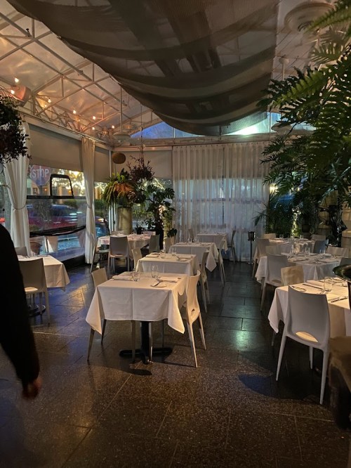 A cozy restaurant interior with white tablecloths, plants, and soft lighting, creating an inviting atmosphere.