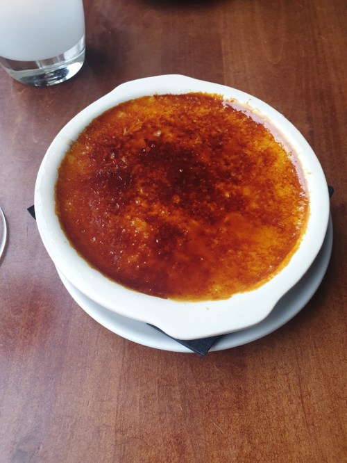 A creamy dessert with a caramelized sugar top, served in a white dish on a wooden table.
