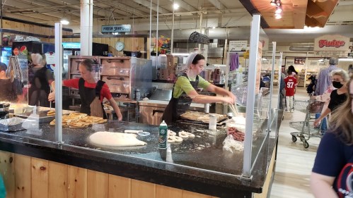 A busy food stall with workers preparing food behind a glass barrier, while customers browse nearby.