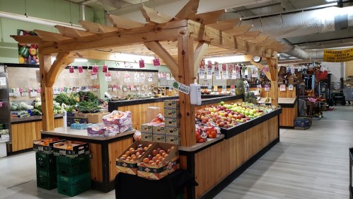 A vibrant market display featuring fresh fruits and vegetables under a wooden structure, with organized produce stands.