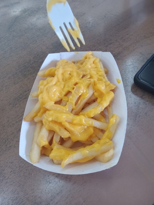 A serving of French fries topped with melted cheese, placed in a white tray on a wooden table.