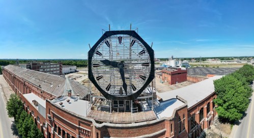 A large clock face on a building rooftop, overlooking an industrial area under a clear blue sky.