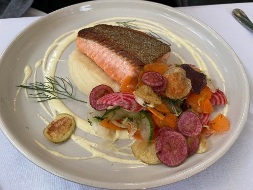 A plate featuring seared salmon on a bed of creamy puree, garnished with colorful vegetable chips and fresh herbs.