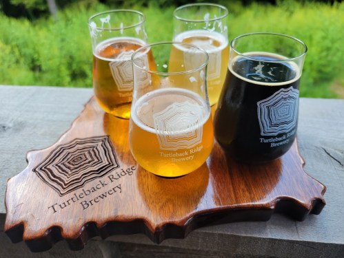 Four glasses of beer in varying colors on a wooden board shaped like a state, labeled "Turtleback Ridge Brewery."