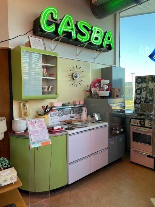 A retro kitchen display featuring pastel-colored appliances and a neon "CASBA" sign.