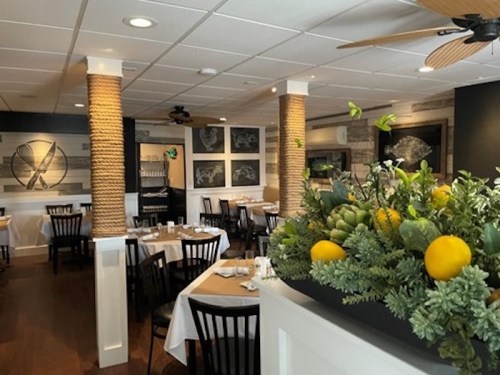 A cozy restaurant interior with tables set, decorative plants, and nautical-themed artwork on the walls.