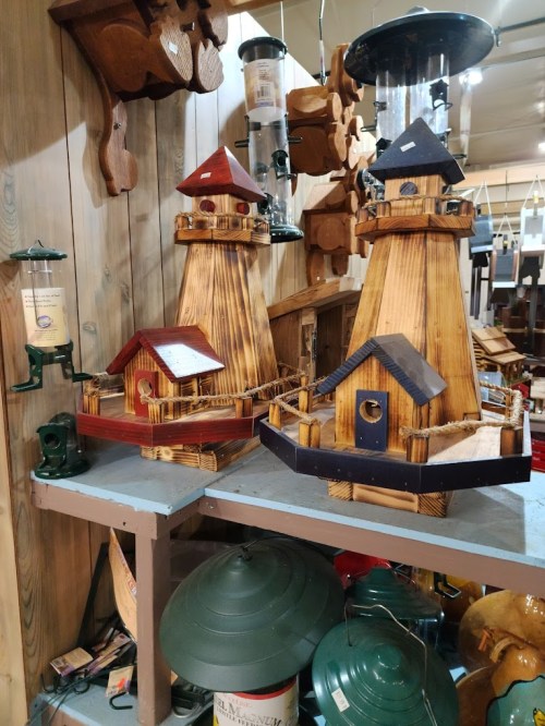 Two wooden lighthouse models in a shop, one red and one blue, displayed on a table among various crafts.