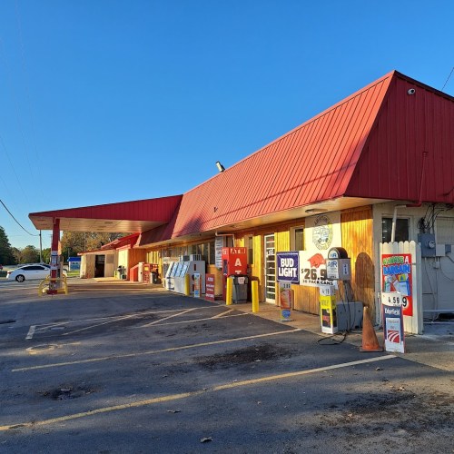 A convenience store with a red roof, featuring gas pumps and various signs, under a clear blue sky.