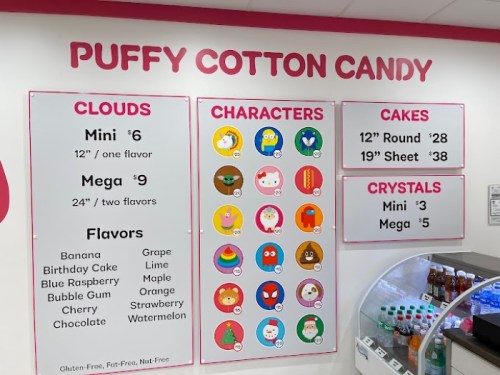 Menu board featuring cotton candy options, flavors, character designs, and cake sizes with prices. Bright and colorful display.