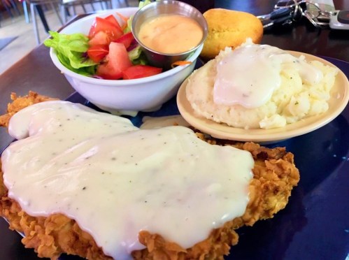 A plate featuring fried chicken smothered in gravy, mashed potatoes, a side salad, and cornbread.