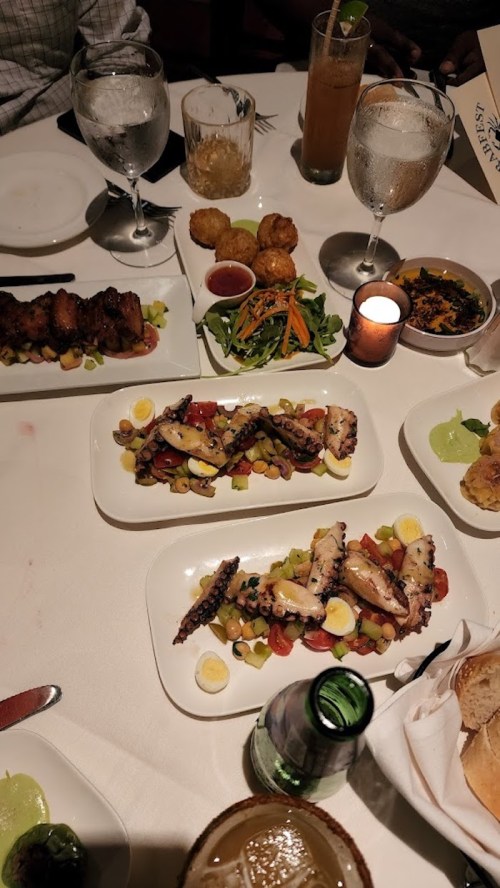 A table set with various dishes, including grilled octopus, salad, and appetizers, with drinks and candles.