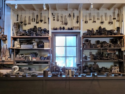 A cluttered workshop with shelves filled with various tools and equipment, and a window letting in natural light.