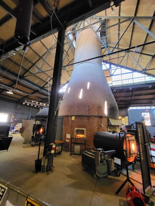A large, brick industrial chimney inside a spacious warehouse, with various equipment and tools around it.