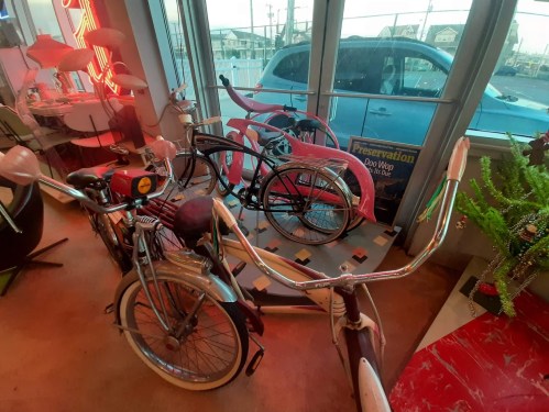 A collection of vintage bicycles displayed indoors, with a blue car visible through the window in the background.