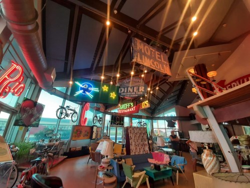 A vibrant retro-themed interior with vintage signs, colorful furniture, and bicycles hanging from the ceiling.