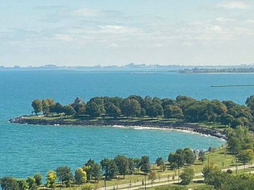 A scenic view of a shoreline with trees, a beach, and calm blue waters under a clear sky.