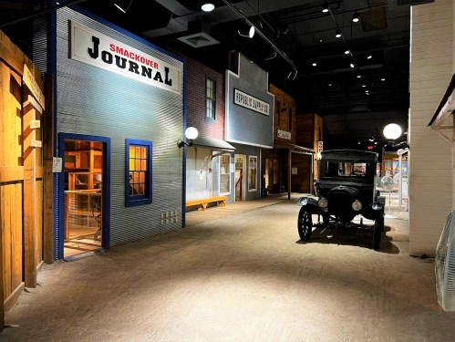 A vintage car parked on a dimly lit street lined with historic storefronts and signs.