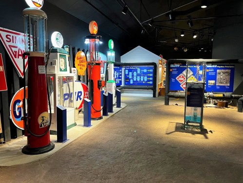 A museum exhibit featuring vintage gas pumps and signage, showcasing automotive history in a dimly lit space.