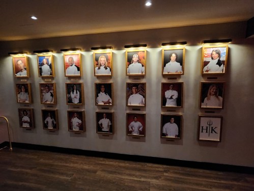 A wall display featuring framed portraits of chefs, each with a nameplate, in a restaurant setting.