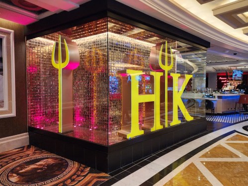 A brightly lit restaurant entrance with large yellow letters "HK" and decorative glass walls in a casino setting.