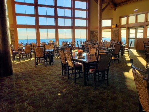 A spacious restaurant with large windows offering a scenic view, featuring tables and chairs arranged neatly.