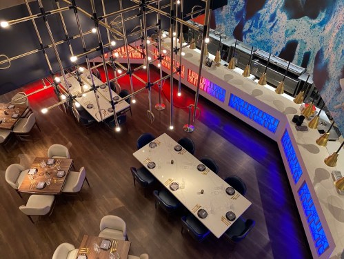 Aerial view of a modern restaurant with stylish tables, colorful lighting, and a sleek bar area.