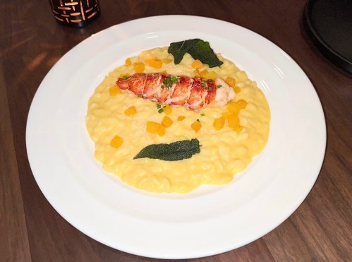 A plate of creamy risotto topped with lobster, butternut squash, and sage leaves, elegantly presented.
