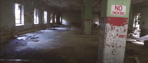 Abandoned room with peeling paint, scattered debris, and a "No Smoking" sign on the wall. Natural light through windows.