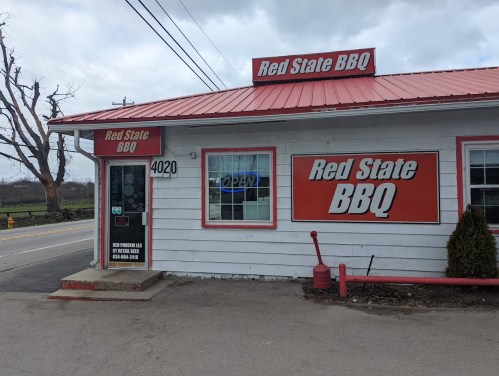 Exterior of Red State BBQ restaurant, featuring a red roof and signage, with a road and trees in the background.