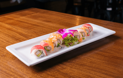 A platter of colorful sushi rolls garnished with a purple flower and green leaves, set on a wooden table.