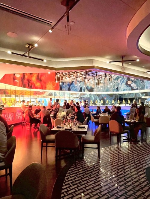 A vibrant restaurant interior with colorful lighting, featuring diners at tables and a stylish bar area.