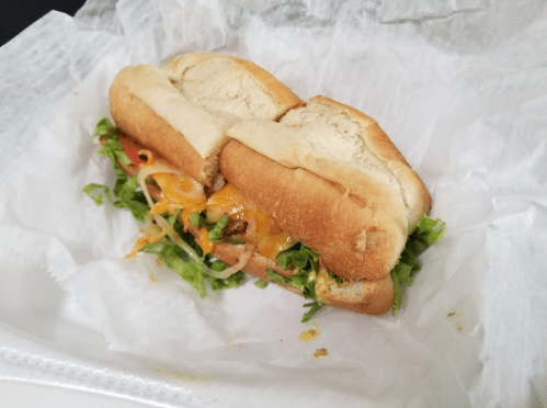 A sandwich with two soft rolls filled with lettuce, tomato, and melted cheese, wrapped in white paper.