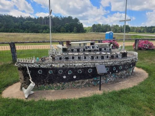 A decorative ship sculpture named "Bremen," made from stones and set in a grassy area with trees in the background.