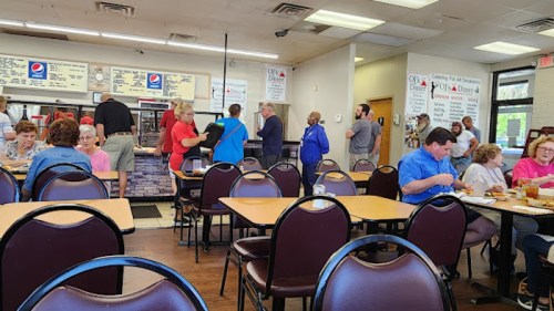 A busy diner interior with customers eating and waiting in line at the counter. Tables are filled with people.