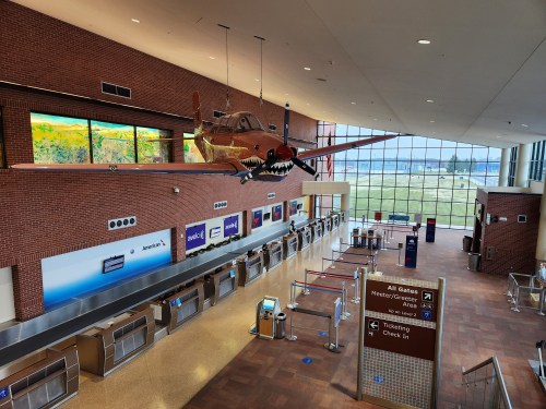 Interior of an airport with a vintage plane hanging from the ceiling, ticketing counters, and large windows.