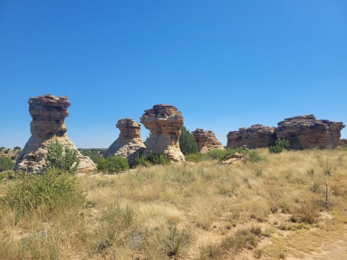 Rock formations rise above a grassy landscape under a clear blue sky.
