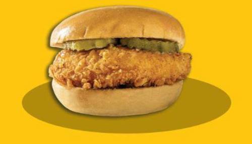 A crispy fried chicken sandwich with pickles on a soft bun, set against a bright yellow background.