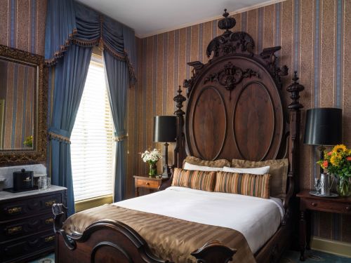 Elegant bedroom featuring a large wooden bed, striped wallpaper, and decorative curtains with floral arrangements.