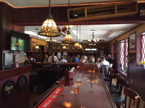 A cozy restaurant interior with a wooden bar, stained glass lamps, and patrons dining at tables in a warm atmosphere.