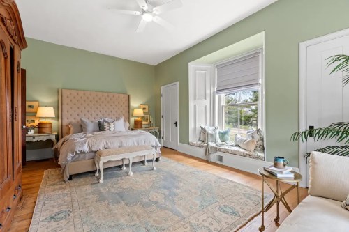 Cozy bedroom with a light green wall, a large bed, decorative pillows, and a window seat with natural light.