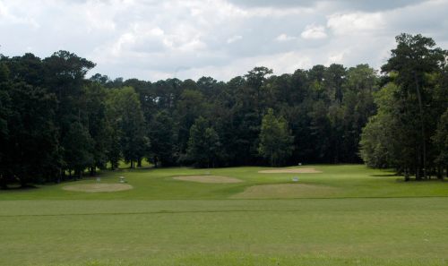 A serene golf course with three practice greens surrounded by lush trees under a cloudy sky.