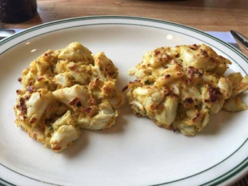 Two golden-brown crab cakes on a white plate, served on a wooden table.