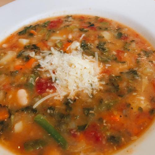 A bowl of hearty vegetable soup topped with grated cheese, featuring colorful vegetables and a rich broth.