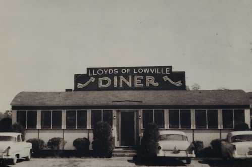 Black and white photo of Lloyd's of Lowville Diner, featuring a classic diner facade and vintage cars parked outside.